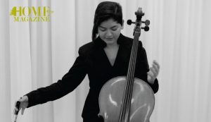 a girl wearing black with a cello in front of her with a hand towards it and the other a little far