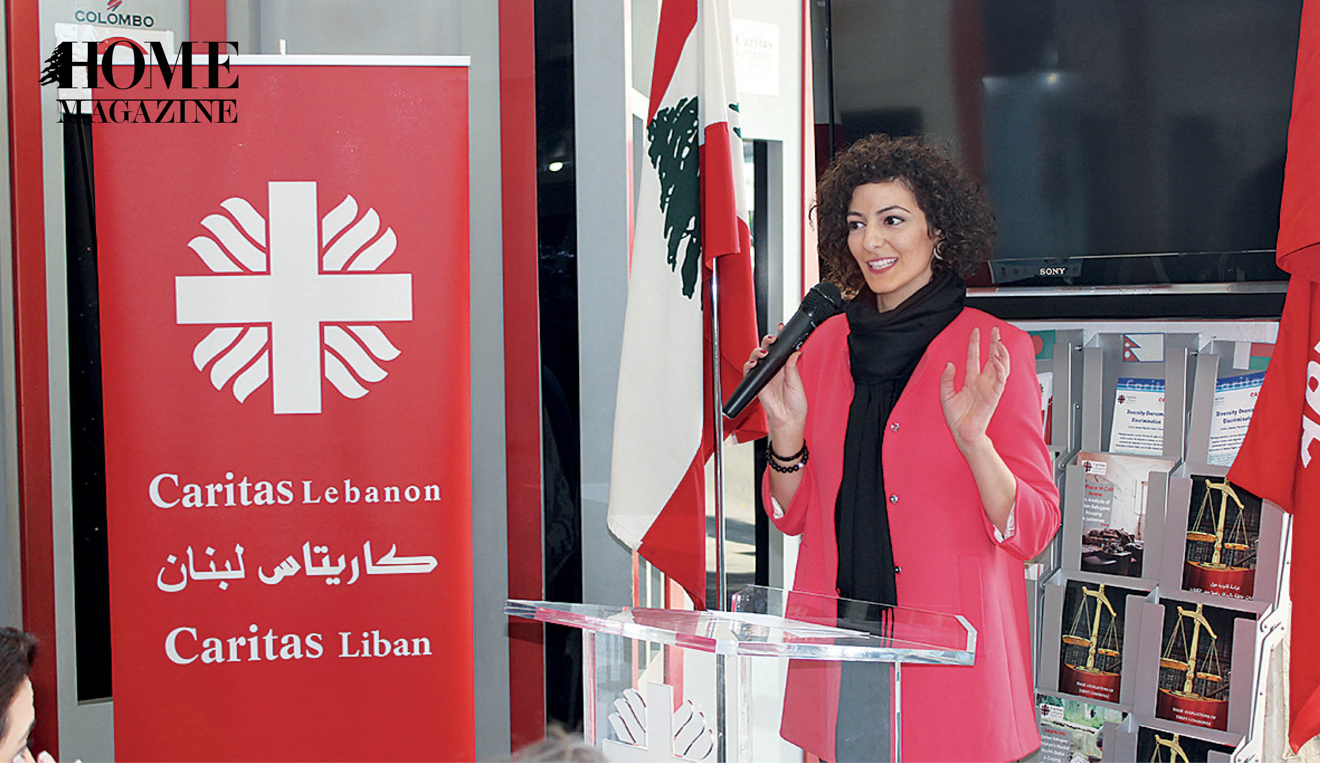Woman speaking on microphone next to Caritas red roll up banner