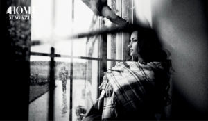 Girl with dark long hair and square-patterned blanket staring out of glass window