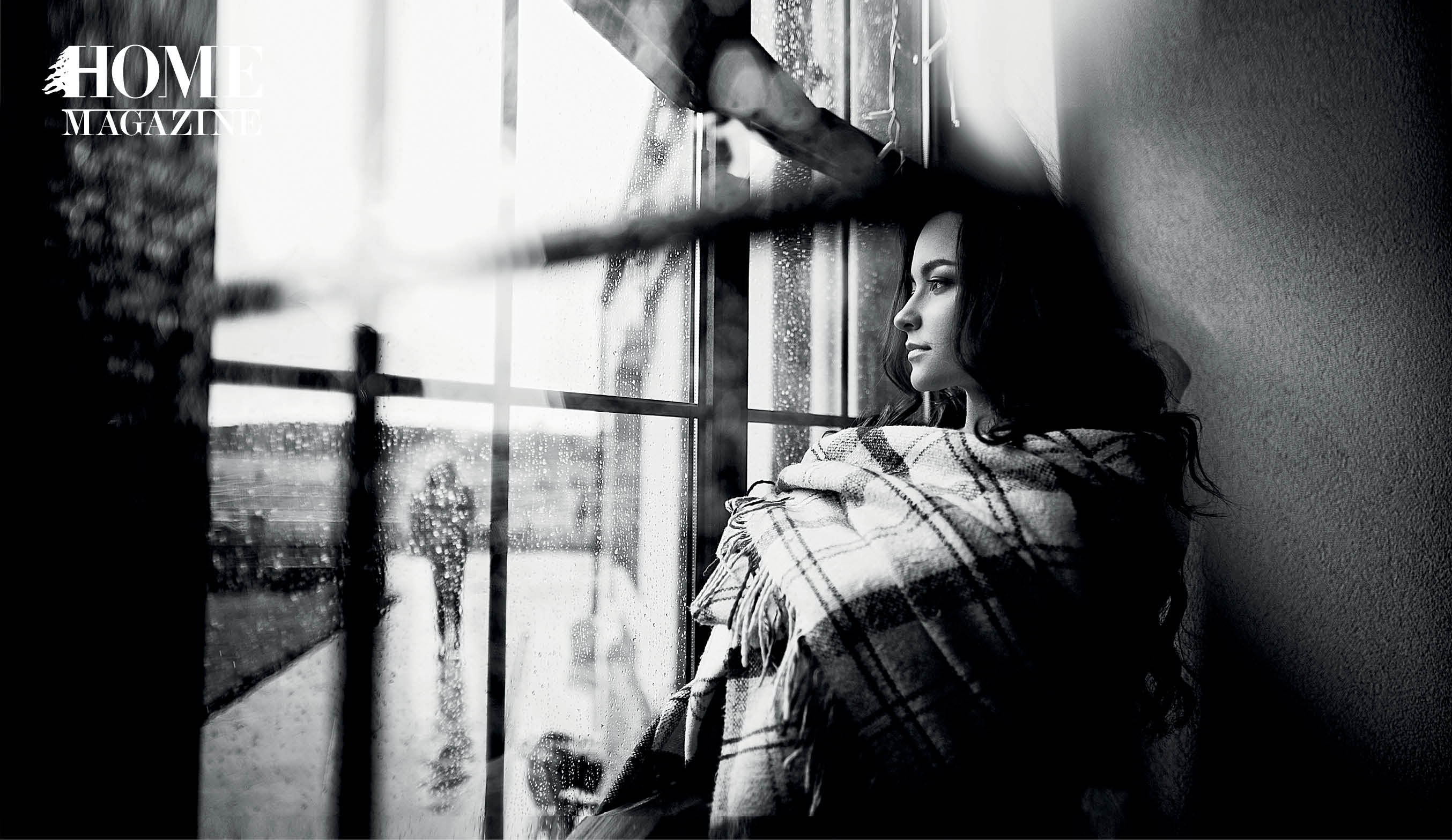 Girl with dark long hair and square-patterned blanket staring out of glass window
