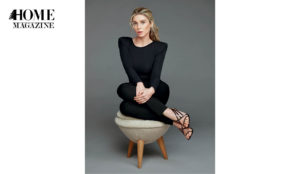 Blond woman in black attire and sandals sitting on a pouf chair