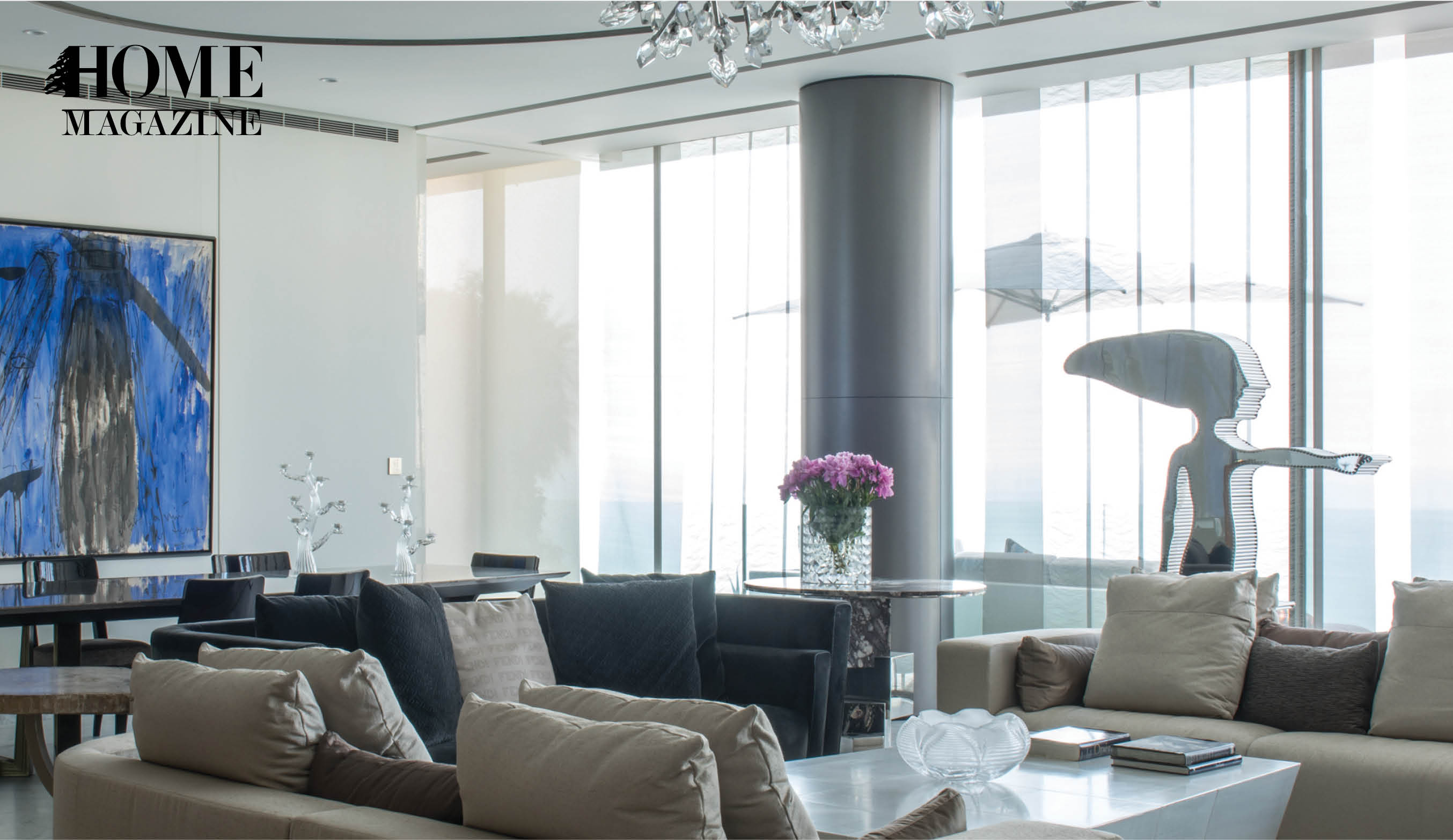 Grey couches in living room, windows, tables, chandelier, and pink flowers in a vase