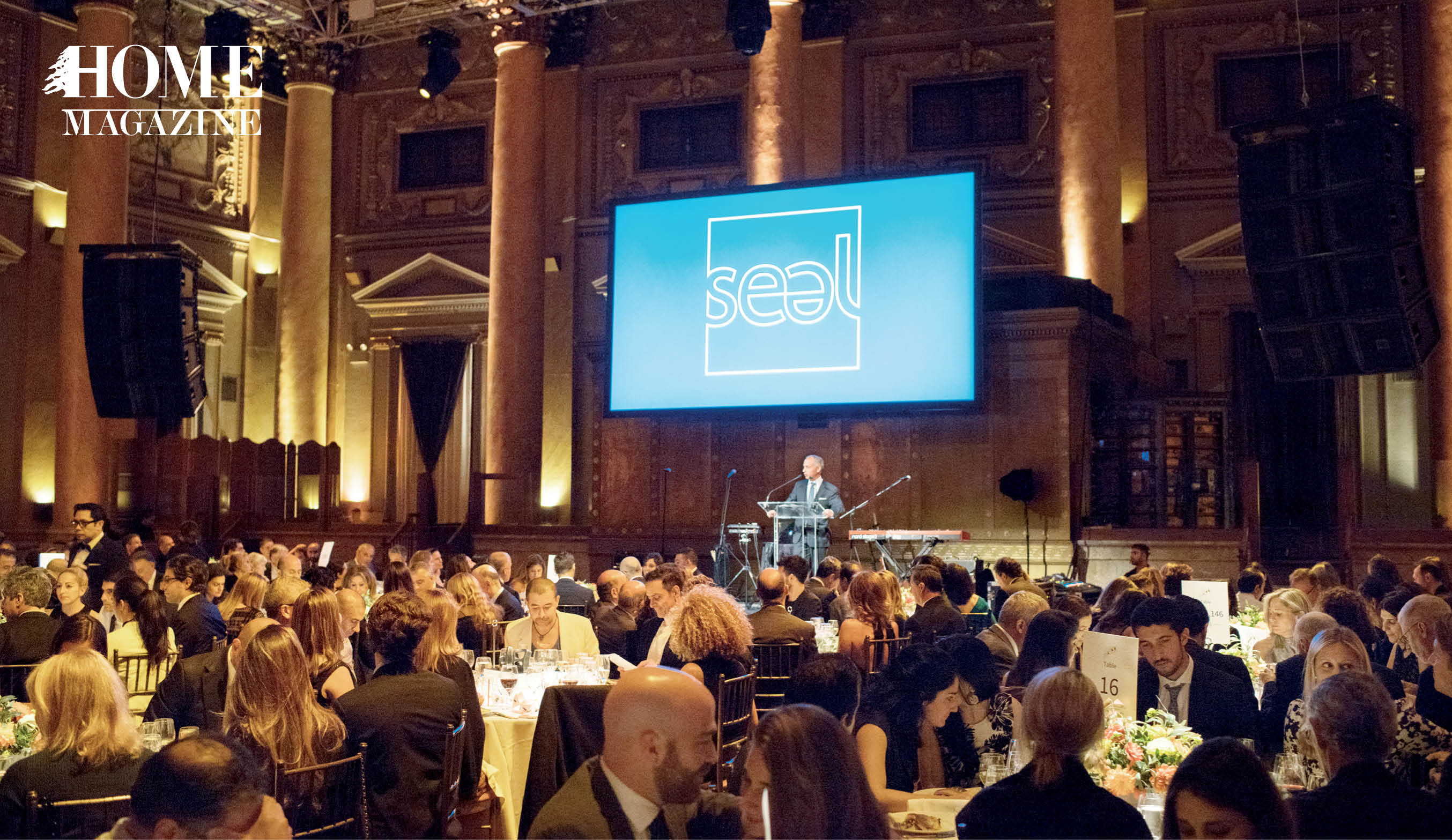 Man speaking in front of blue screen and seated audience