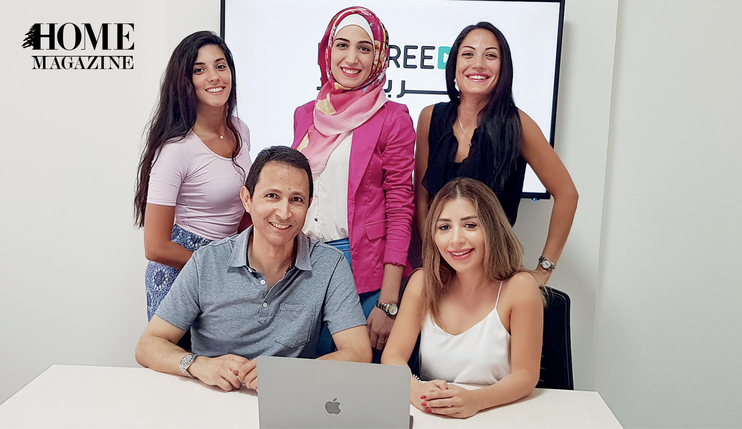 Group of 4 women and 1 man in front of a digital board and laptop on a desk