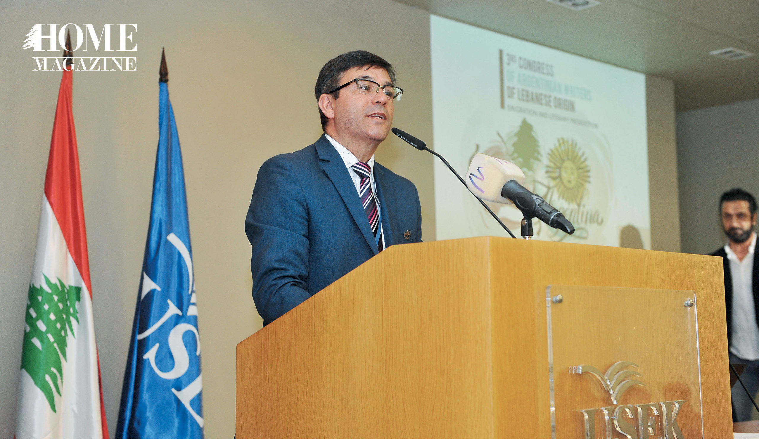 Man wearing suit and eyeglasses giving speech on microphone stand
