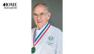Man of grey hair and eye glasses wearing a medal and a white coat
