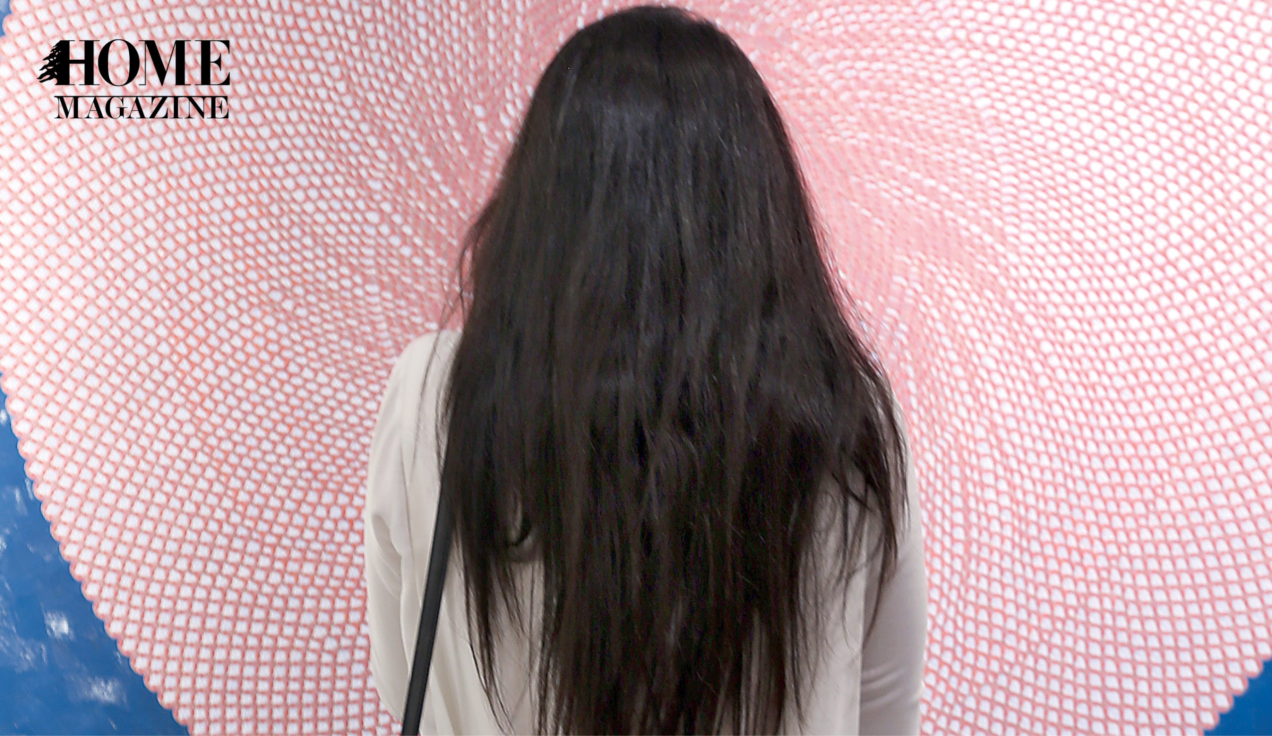 Back shot of woman with long black hair standing facing a pink circular object