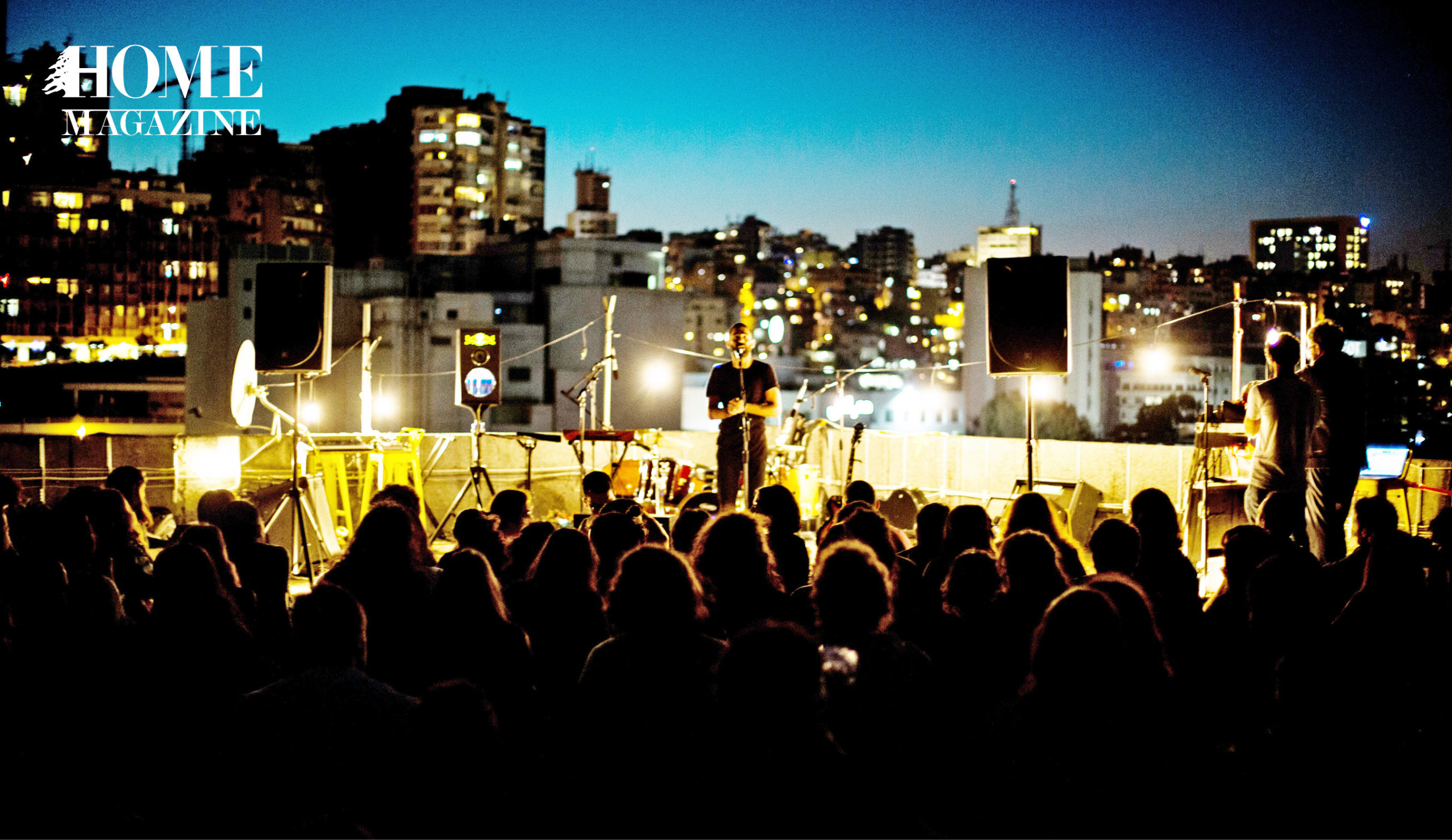 Man performing on stage with crowd and buildings and lights behind him