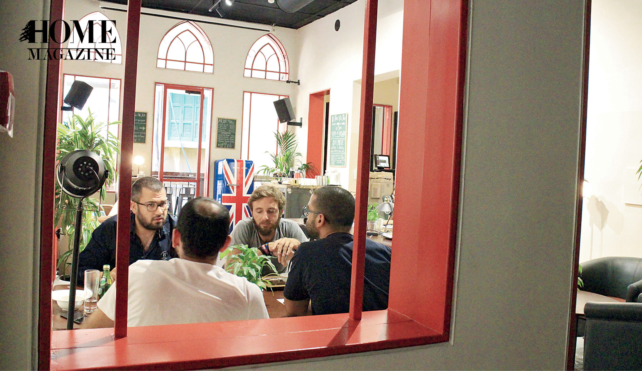Four man gathering around table behind red wood window