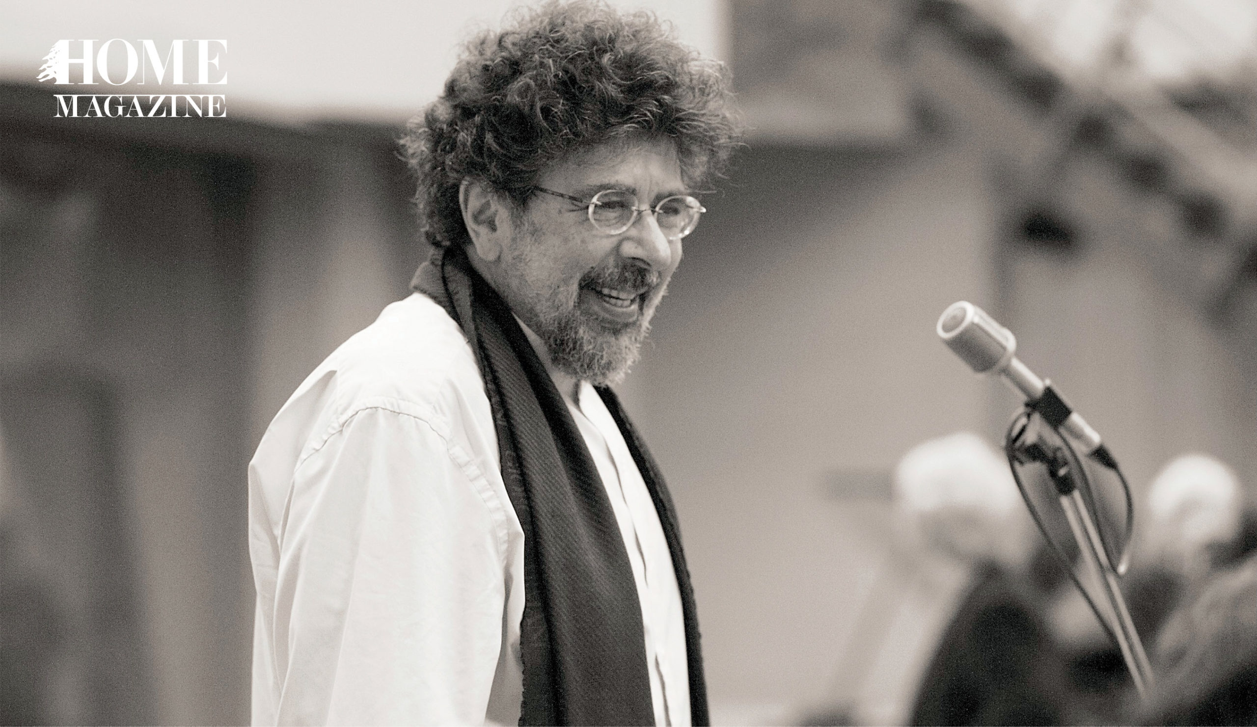 Man wearing white shirt, scarf and eyeglasses standing in front of microphone