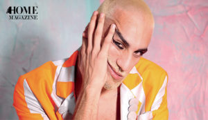 Face portrait of a bold man with an orange colored shirt with his hand on his face