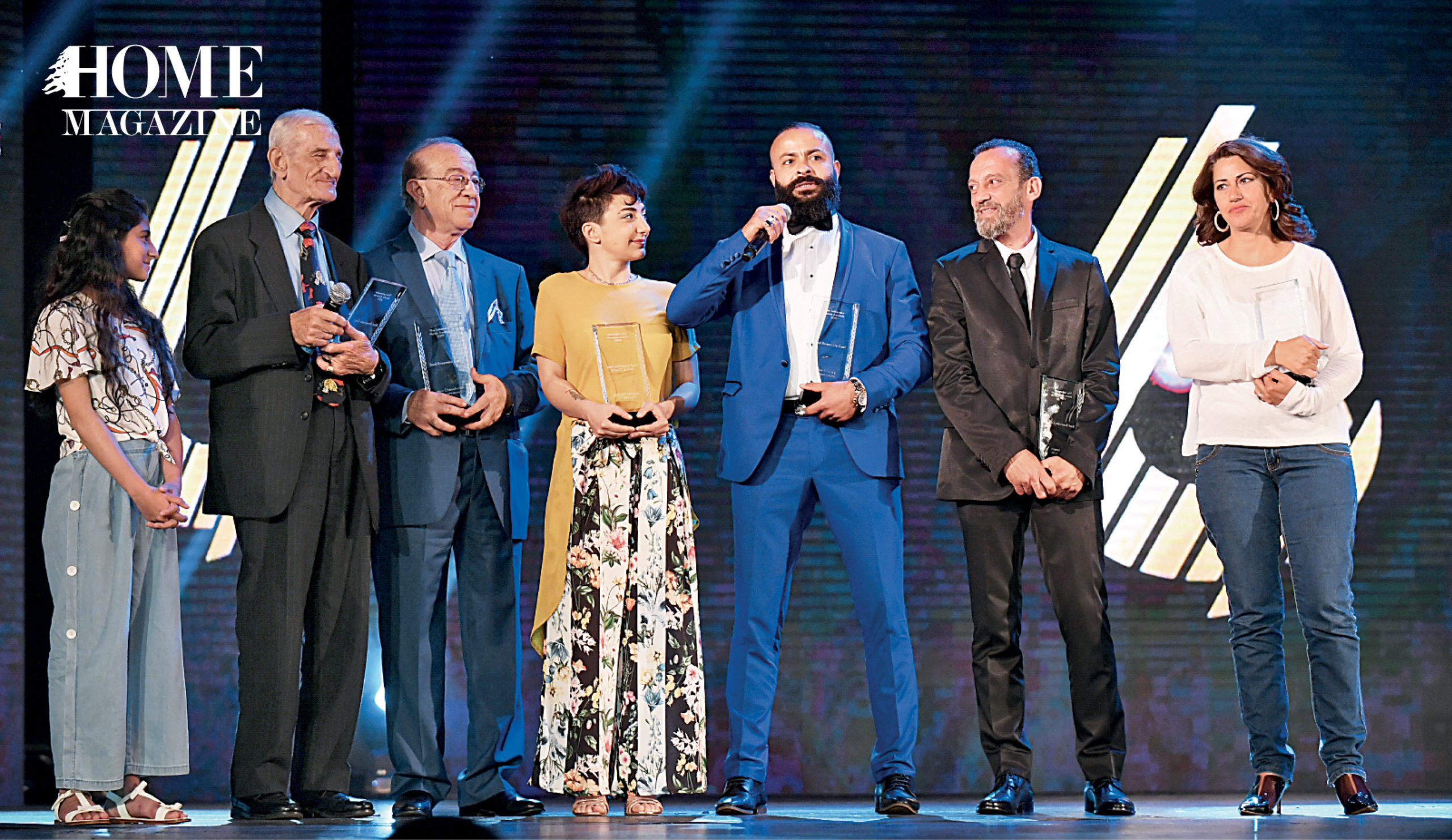Group of men and women in stage among whom a man in navy suit is giving a speech in center